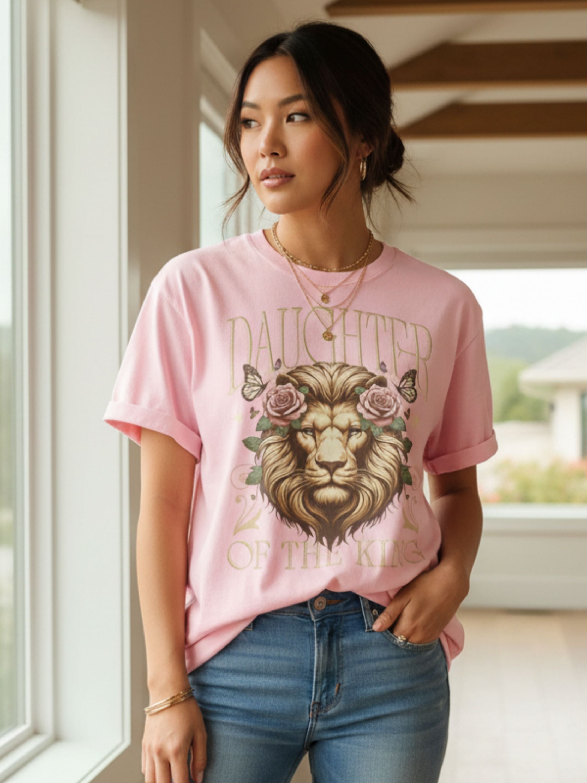 Woman wearing a pink t-shirt with a lion graphic and text, standing indoors.