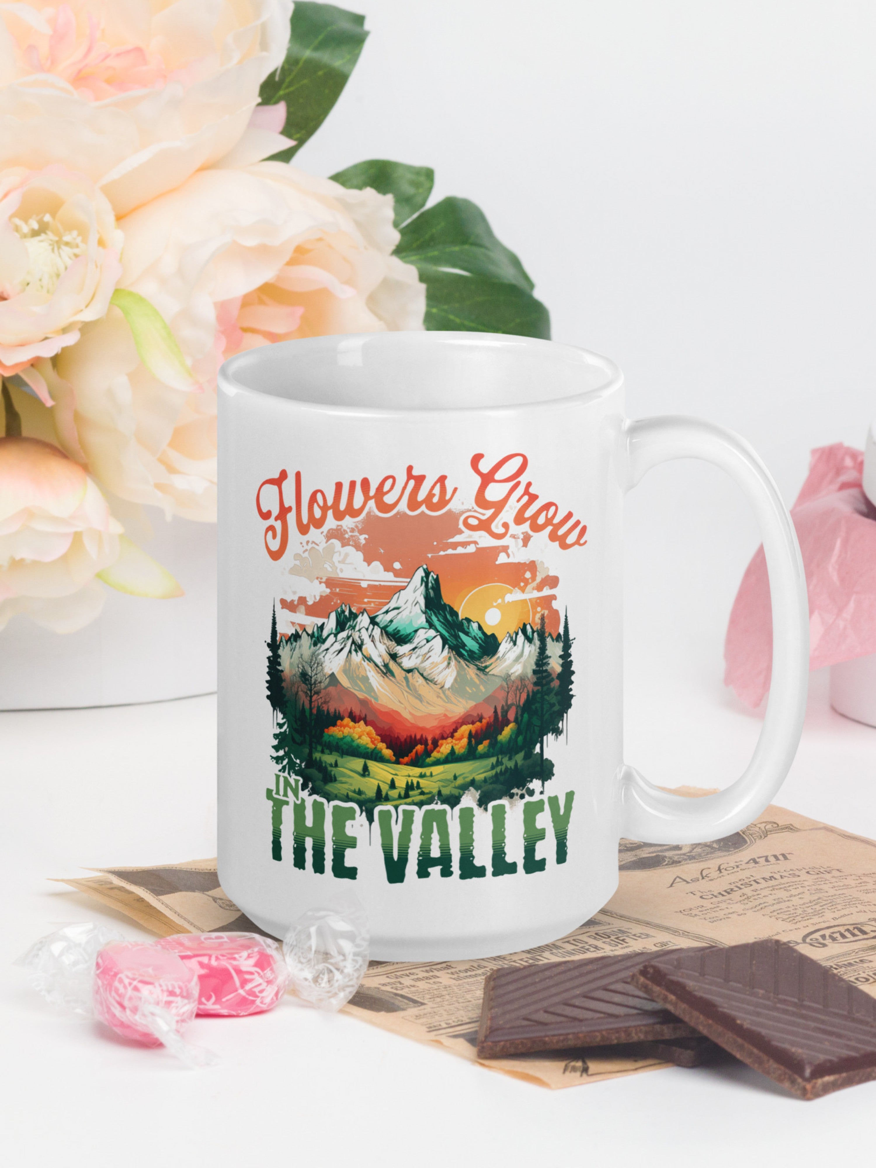 White mug with mountains and 'Flowers Grow in the Valley' scenic artwork in a natural setting