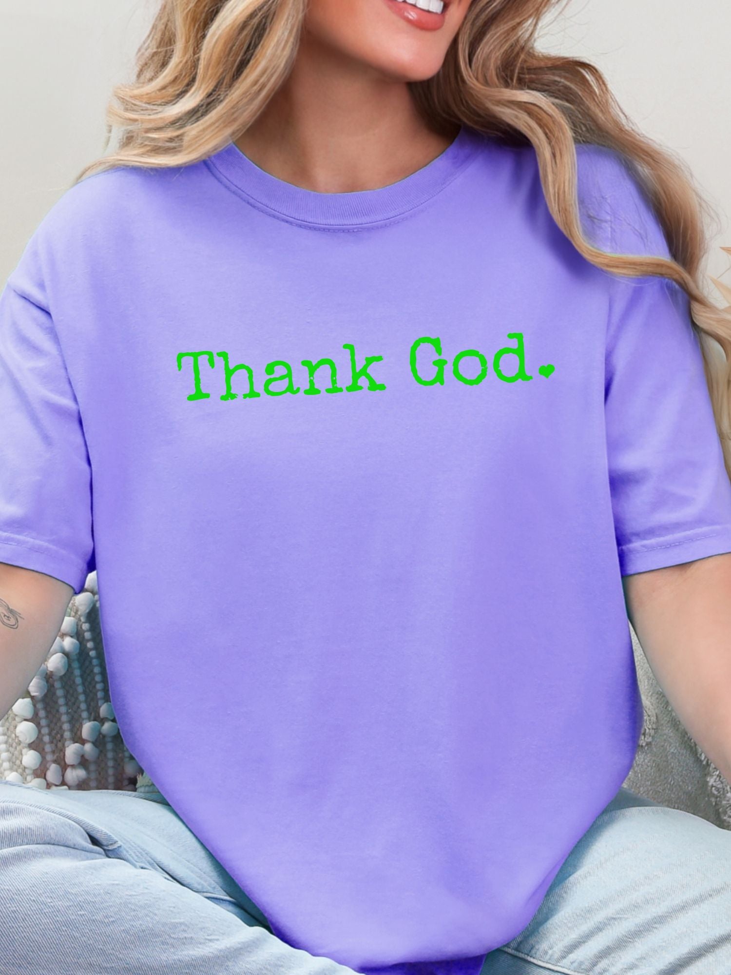Woman wearing a purple shirt with 'Thank God.' in green text.