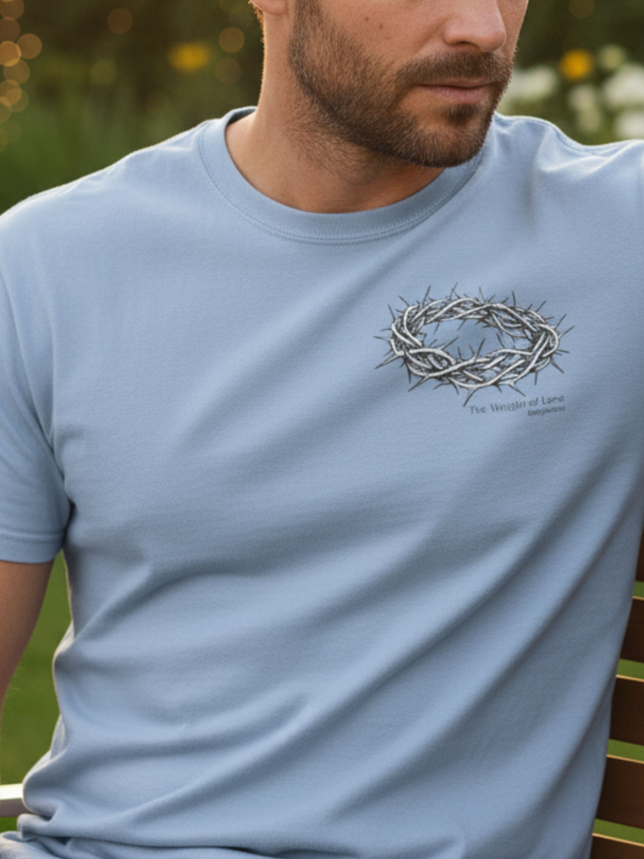 Man wearing a light blue t-shirt with a crown of thorns design outdoors.