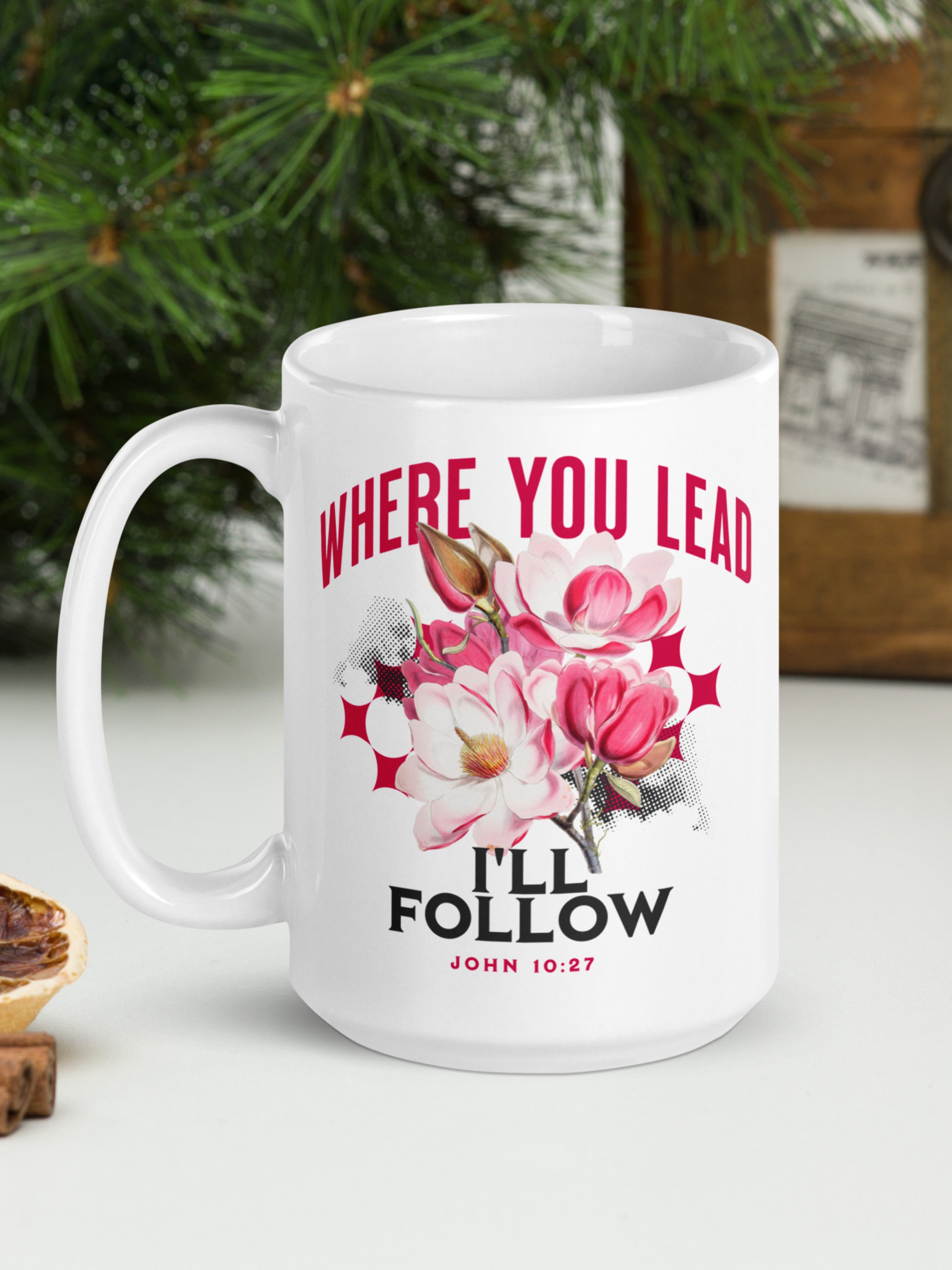 White mug with floral design and text 'Where you lead, I'll follow' on a white surface with greenery in the background.