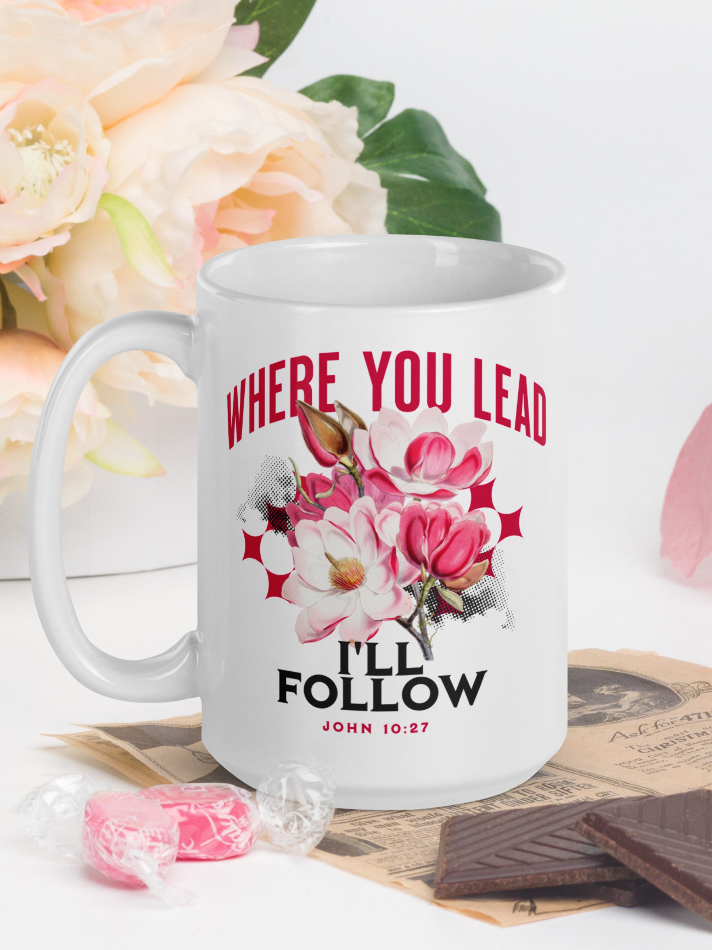 White mug with floral design and text 'Where you lead, I'll follow' on a table with flowers and chocolate.