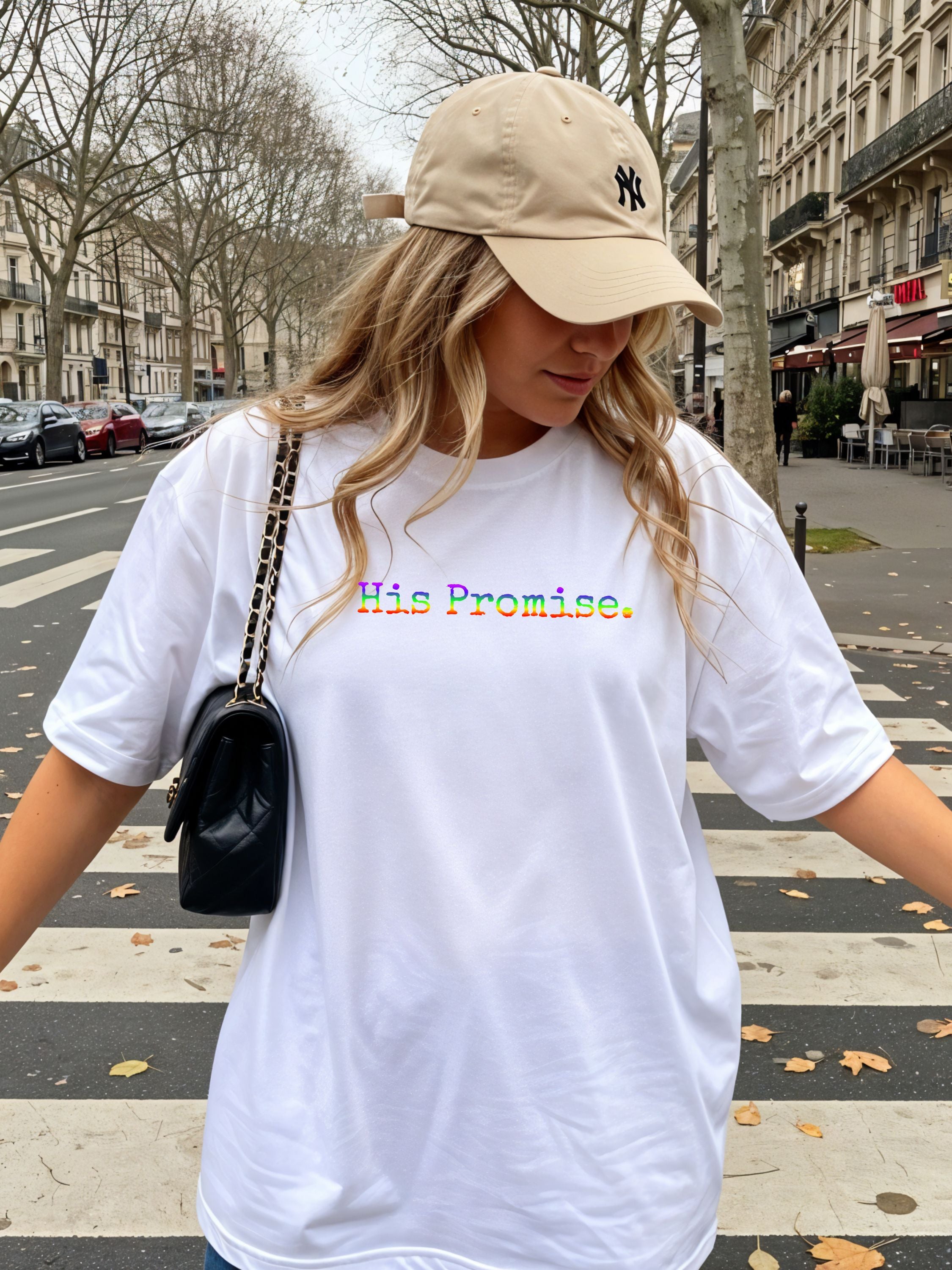 Person wearing a white t-shirt with 'His Promise' text in rainbow letter on a city street.