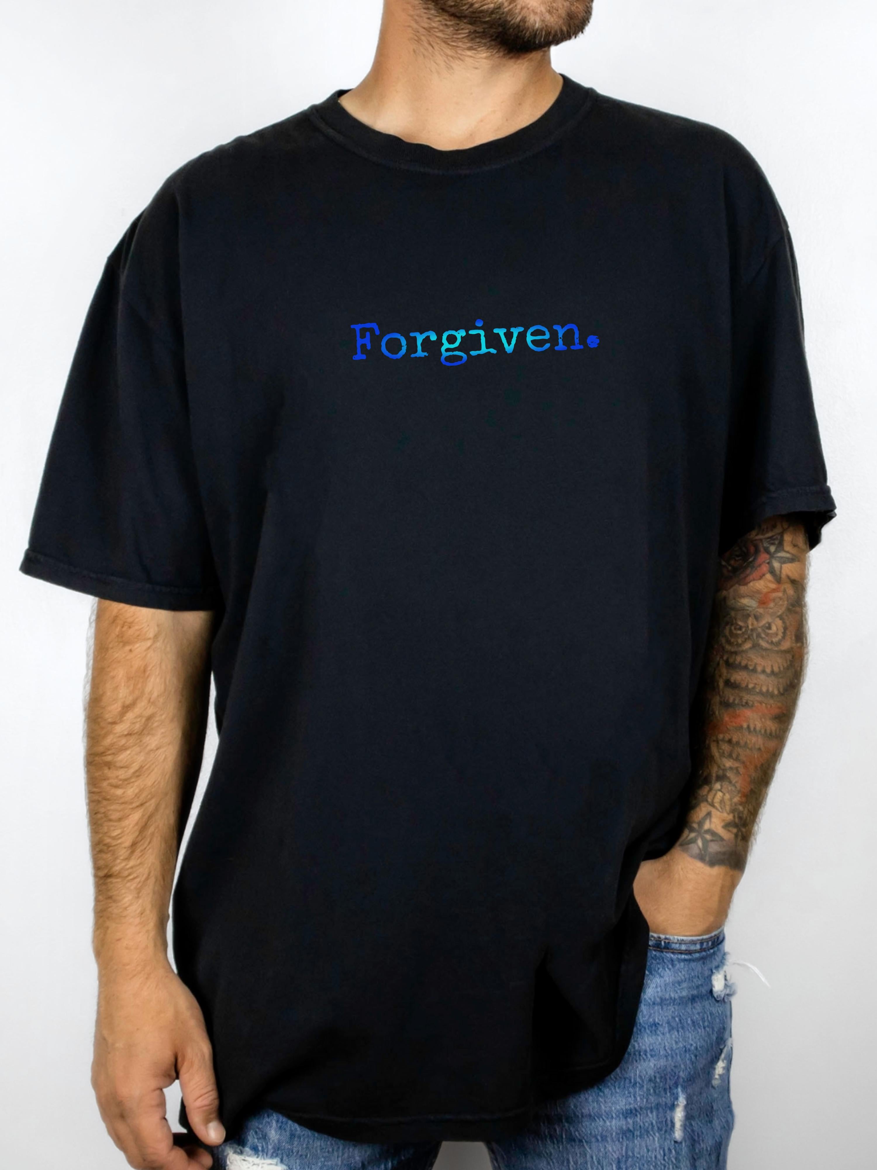 Person wearing a black t-shirt with shades of blue 'Forgiven.' text printed on it.
